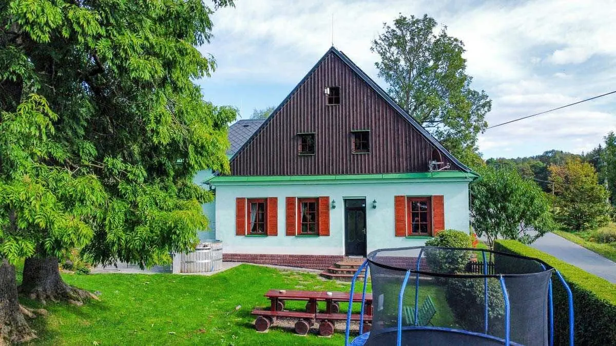 Štít zahradní strany v létě, před domem lavice a trampolína