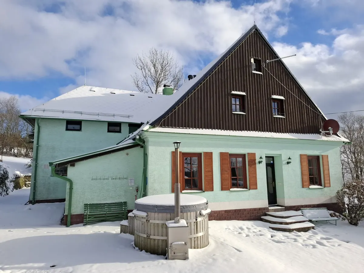 Zahradní strana Severky ráno ve sněhu: mátová fasáda, okenice a sud pod termokrytem