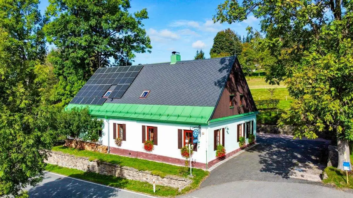 Severka shora v létě: fotovoltaika na střeše, mátová fasáda a cedule s hvězdou u vchodu