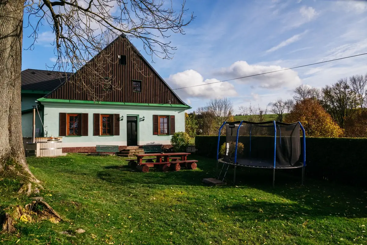 Zahradní strana Chaty Severky: trávník, stůl z kulatin, trampolína a koupací sud u domu