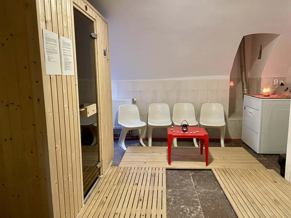 Infrasauna se skleněnými dveřmi a odpočívárna s bílými křesly a červeným stolkem s aromalampou