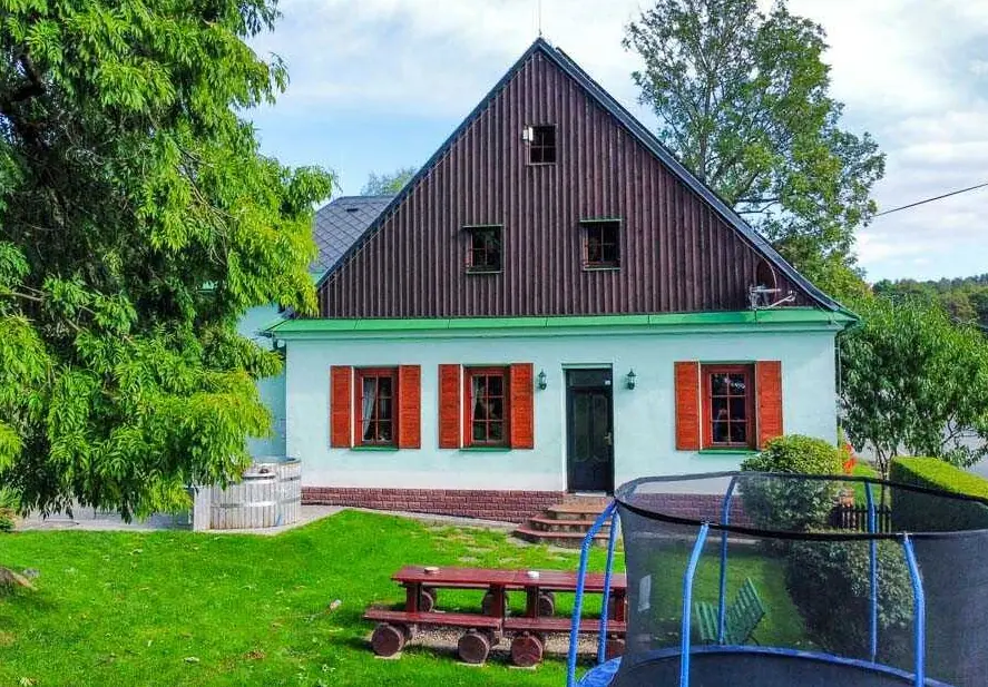 Zahradní štít Severky v létě ze stejného místa: zelený trávník, stůl z kulatin a vlevo sud