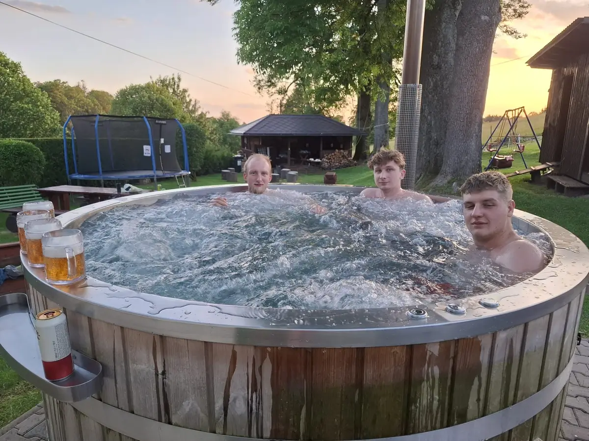 Hosté v sudu s pivem při západu slunce, za nimi trampolína a altán